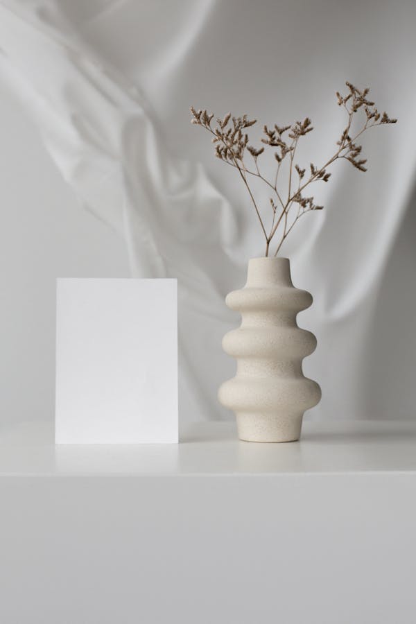 Elegant minimalistic setup with ceramic vase and blank card on white background.