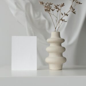 Elegant minimalistic setup with ceramic vase and blank card on white background.